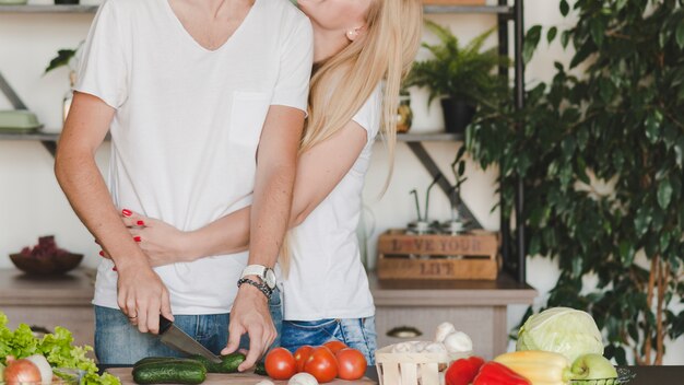 Kobieta obejmuje jej chłopaka tnących warzywa z nożem na kuchennym kontuarze