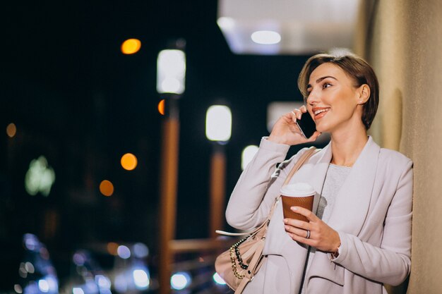 Kobieta opowiada na telefonie i pije kawę outside w ulicie przy nocą