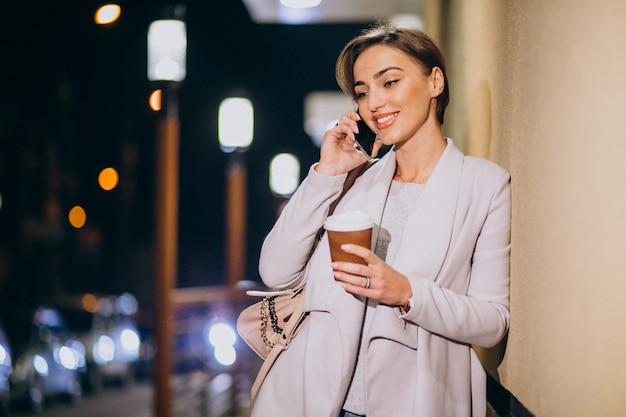 Kobieta Opowiada Na Telefonie I Pije Kawę Outside W Ulicie Przy Nocą