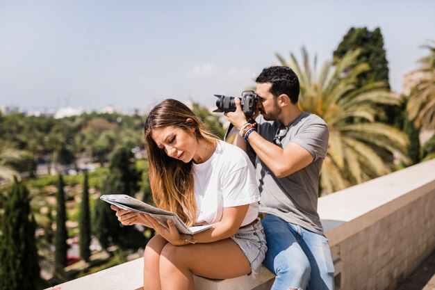 Kobieta patrzeje mapy obsiadanie z jej chłopakiem bierze fotografię na kamerze w parku