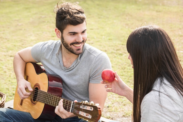 Kobieta patrzeje mężczyzna bawić się gitarę w parku
