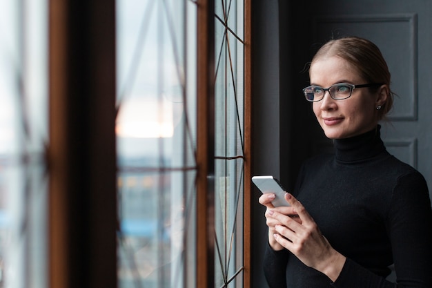 Bezpłatne zdjęcie kobieta patrzeje na okno z telefonem