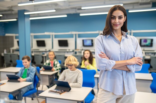 Kobieta pewnie patrząca na kamerę i siedzących z tyłu studentów