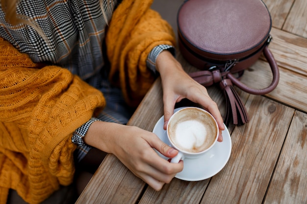 Kobieta pije kawę. Stylowa torba na stół. Ubrana w szarą sukienkę i pomarańczową kratę. Przyjemny poranek w kawiarni.