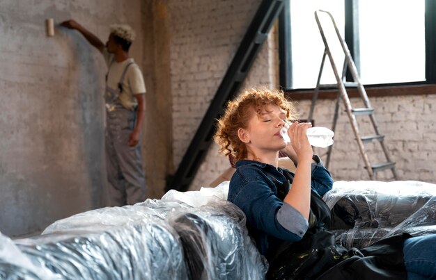 Kobieta pije wodę, podczas gdy mężczyzna maluje ścianę swojego nowego domu
