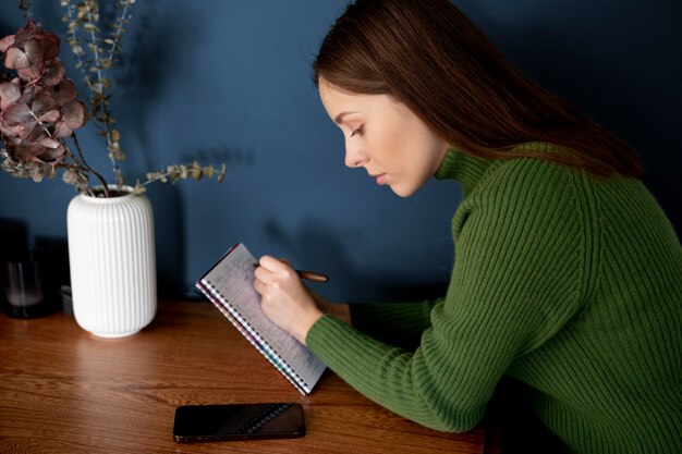 Bezpłatne zdjęcie kobieta pisze coś na zeszycie obok swojego smartfona