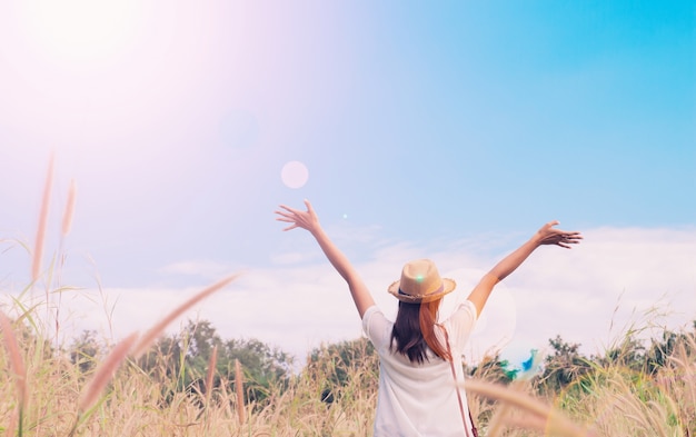 Kobieta podróżnik z aparatu fotograficznego gospodarstwa kapelusz i oddychanie w polu trawy i lasu, koncepcja podróży wanderlust, miejsce na tekst, moment epicki