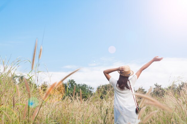 Kobieta podróżnik z aparatu fotograficznego gospodarstwa kapelusz i oddychanie w polu trawy i lasu, koncepcja podróży wanderlust, miejsce na tekst, moment epicki