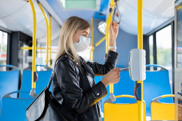 Kobieta podróżująca autobusem publicznym w masce medycznej dla ochrony i korzystająca z biletu autobusowego