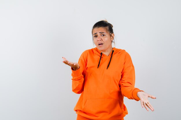 kobieta pokazująca bezradny gest w pomarańczowej bluzie z kapturem i wyglądająca na zdezorientowaną
