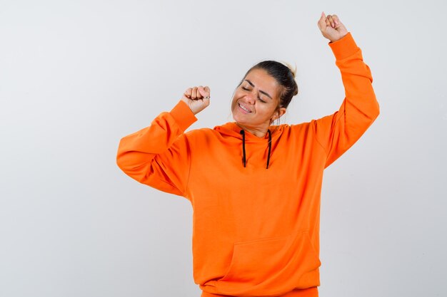 kobieta pokazująca gest zwycięzcy w pomarańczowej bluzie z kapturem i wyglądająca na szczęśliwą