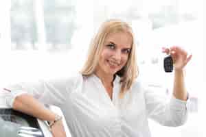 Bezpłatne zdjęcie kobieta pokazuje samochodowych klucze i patrzeje kamerę