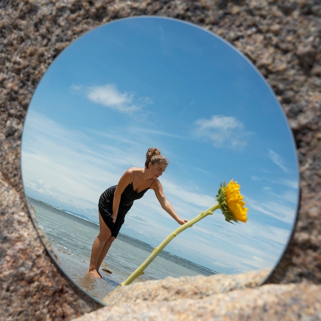 Bezpłatne zdjęcie kobieta pozuje z okrągłym lustrem i kwiatem