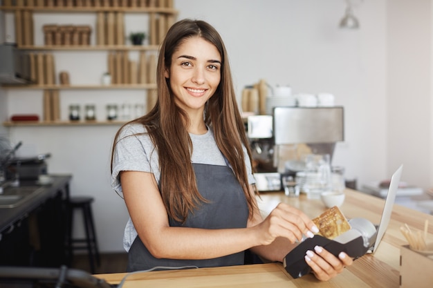 Bezpłatne zdjęcie kobieta pracownik kawiarni za pomocą czytnika kart kredytowych wystawiać rachunek na klienta patrząc szczęśliwy uśmiechając się do kamery.