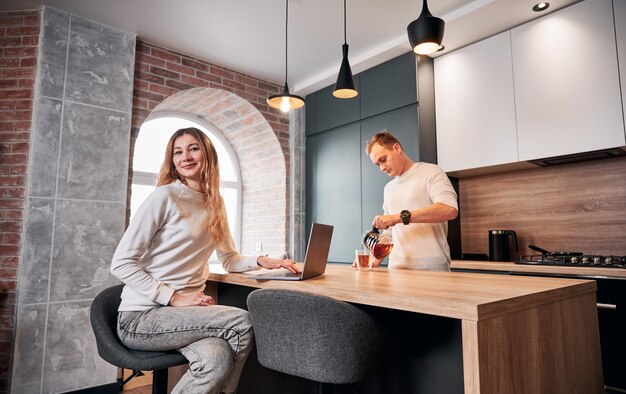 Kobieta pracuje na laptopie, podczas gdy mężczyzna robi herbatę