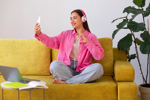 Bezpłatne zdjęcie kobieta prowadząca rozmowę wideo na smartfonie, siedząc na kanapie w domu