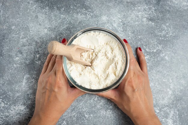 Kobieta ręka trzyma szklaną miskę mąki na marmurze.