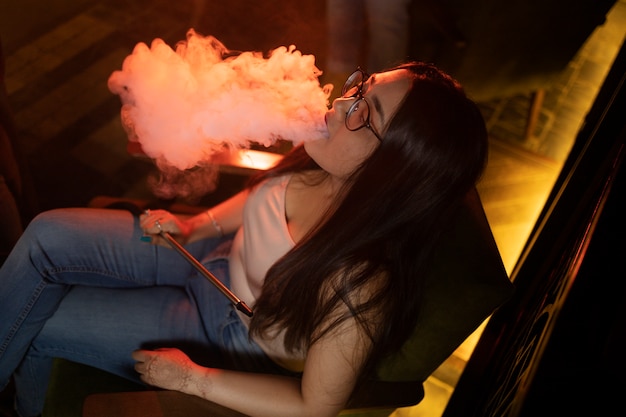 Bezpłatne zdjęcie kobieta relaksująca się przez vaping z fajki wodnej w barze