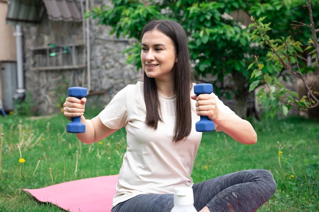 Kobieta rozciągająca się z hantlami robi ćwiczenia fitness w zielonym parku