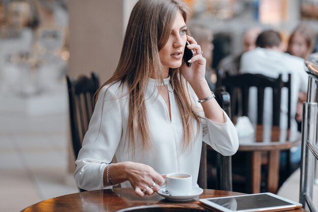 Kobieta rozmawia przez telefon i trzyma kubek kawy