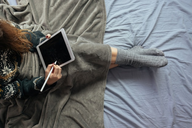 Bezpłatne zdjęcie kobieta rysująca na czarnym ekranie tabletu siedząc na łóżku przykrytym kocem