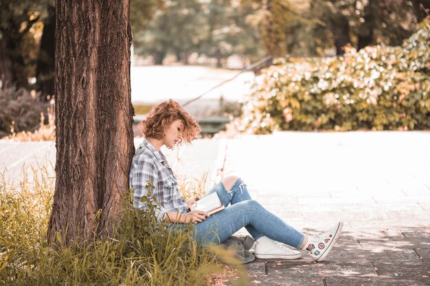 Kobieta siedzi blisko drzewa i czytelniczej książki