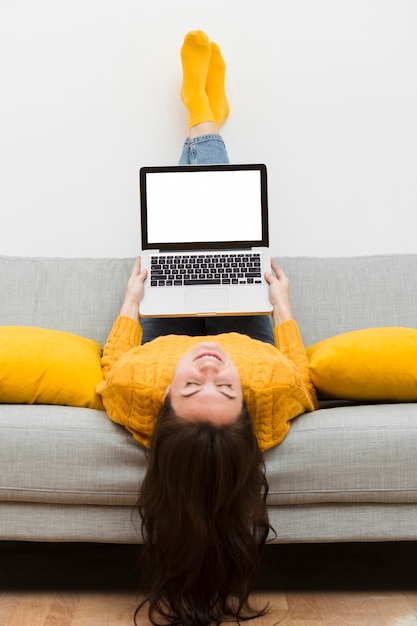 Bezpłatne zdjęcie kobieta siedzi do góry nogami na sodzie i trzyma laptopa na kolanach