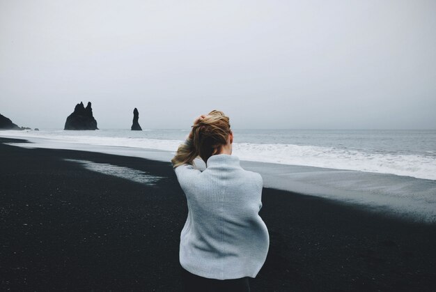Kobieta siedzi na brzegu w pobliżu wody z pochmurnego nieba w tle strzał z tyłu