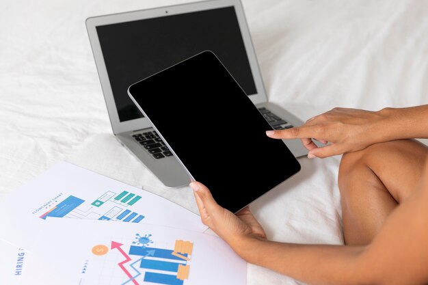 Kobieta siedzi na łóżku z laptopem i tabletem
