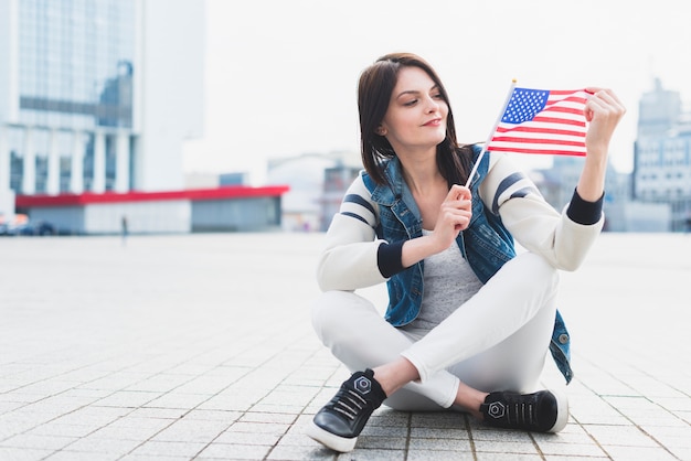 Kobieta siedzi na placu i trzymając w ręku amerykańską flagę