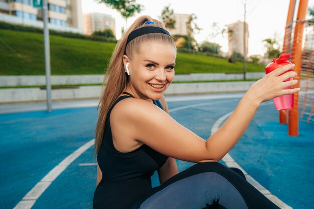 Kobieta siedzi na placu zabaw z butelką wody