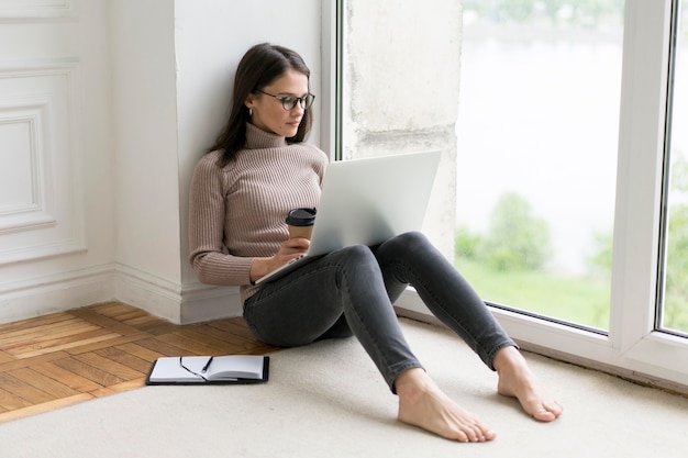 Kobieta siedzi na podłodze i pracuje na swoim laptopie