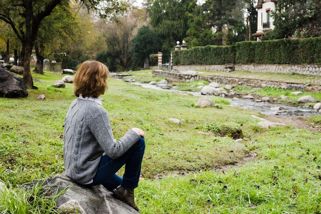 Kobieta siedzi na skale w pobliżu rzeki