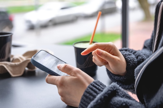 Bezpłatne zdjęcie kobieta siedzi na tarasie kawiarni i używa zbliżenia smartfona