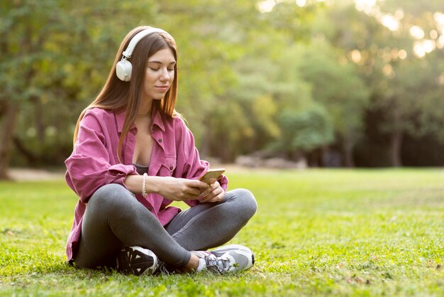 Kobieta siedzi na trawie i sprawdza swój telefon