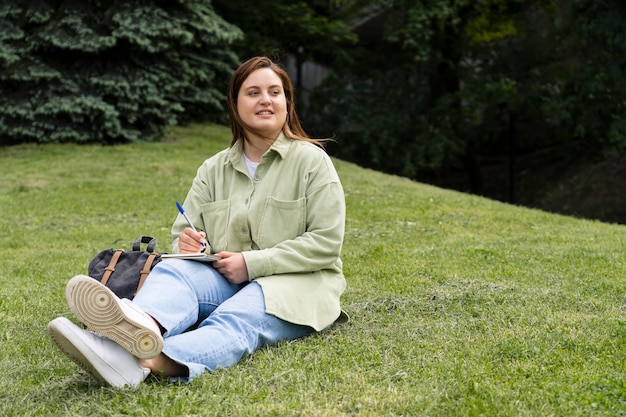 Kobieta siedzi na trawie w pełnym ujęciu