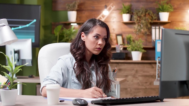 Kobieta siedzi przy biurku, pisząc pomysły na projekty na notebooku analizując prezentację zarządzania pracy w strategii firmy w biurze uruchamiania. menedżer wykonawczy planujący współpracę biznesową