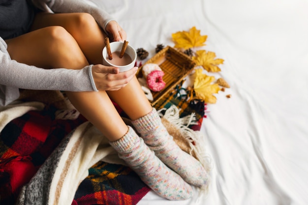 kobieta siedzi w łóżku z książkami i pije kawę z cynamonem, ciastkami i pączkami z lukrem.