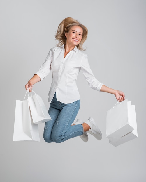 Kobieta skacze i pozuje, trzymając mnóstwo toreb na zakupy