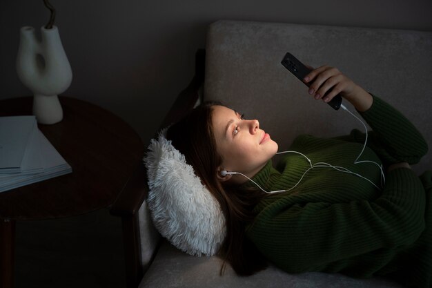 Kobieta słucha muzyki i patrzy na swojego smartfona leżąc na łóżku
