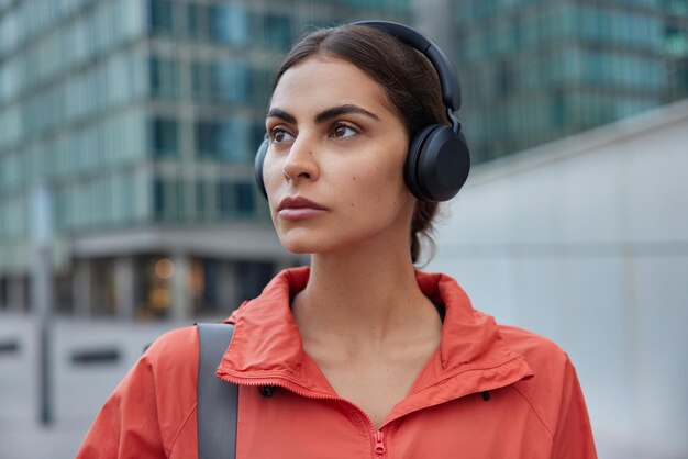 kobieta słucha muzyki w bezprzewodowych słuchawkach słucha ścieżki dźwiękowej ubrana w kurtkę czeka na trenera pozuje na zewnątrz