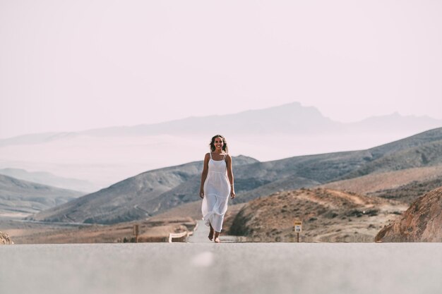 Kobieta spacerująca po drodze w pobliżu wzgórz pod zachmurzonym niebem