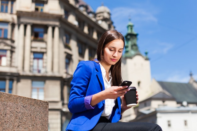 Kobieta sprawdza jej telefonu siedzi z filiżankę kawy na ulicy