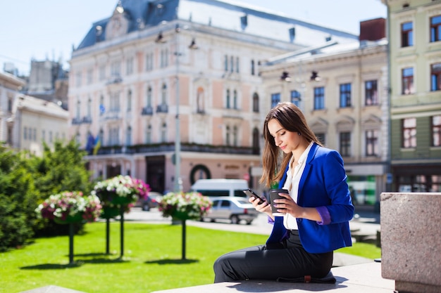 Kobieta sprawdza jej telefonu siedzi z filiżankę kawy na ulicy