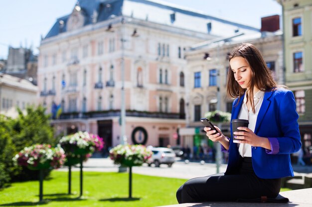 Kobieta sprawdza jej telefonu siedzi z filiżankę kawy na ulicy