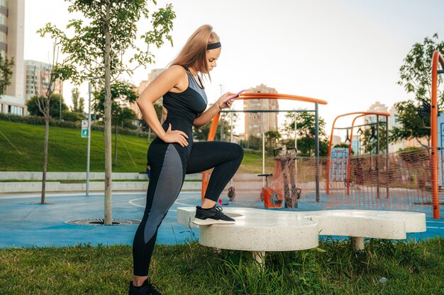 Kobieta stoi na siłowni na świeżym powietrzu z telefonem