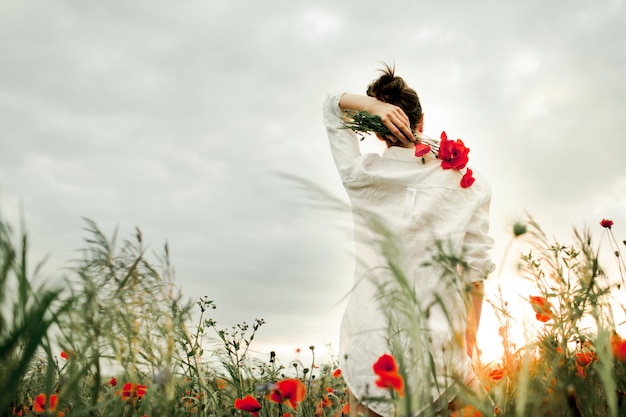 Kobieta stoi z bukietem kwiatów maku na plecach, wśród łąki