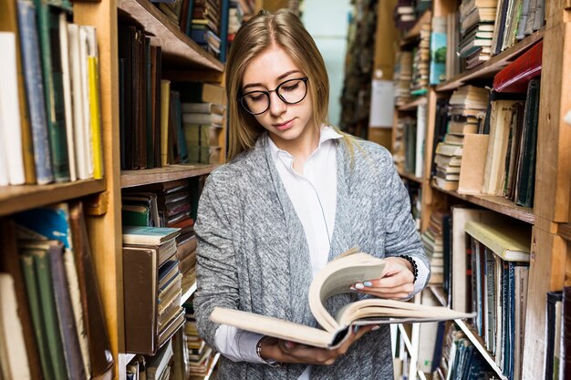 Kobieta stojąca między biblioteczkami i przewracającymi się stronami książek