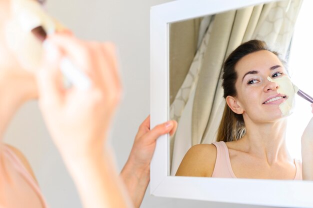 Kobieta stosuje twarzy maskę podczas gdy patrzejący w lustrze