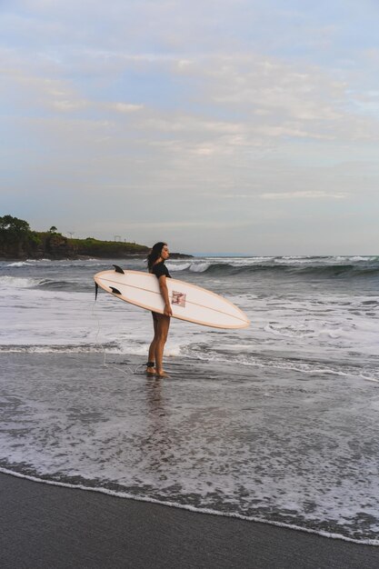 Kobieta surfer z deską surfingową na oceanie o zachodzie słońca